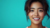 Young Asian woman with bright genuine smile and natural makeup against turquoise background, messy updo hairstyle showing confidence and joy in casual portrait.