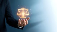 Businessman in dark suit holding glowing scales of justice symbol with light particles, representing law, legal services, fairness, and compliance for corporate and business concepts.