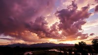 Dramatic purple and pink storm clouds at sunset over mountain landscape with golden light breaking through atmospheric sky creating moody evening scenery.