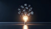 Glowing light bulb with floating business icons representing innovation, creativity and entrepreneurship concepts on dark background.