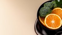 Fresh broccoli florets and sliced orange citrus fruit arranged in black bowl on neutral background. Healthy eating and nutrition concept.