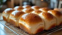 Fresh homemade milk bread rolls with golden brown crust arranged in rows on cooling rack, showing soft texture and professional bakery quality for food photography.