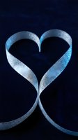 Silver glitter ribbon twisted into a heart shape on dark blue velvet background, romantic symbol for Valentine's Day and love concepts.