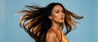 Young mixed-race woman with flowing brown hair in motion against blue sky background, expressing freedom and vitality in golden hour light.
