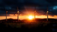 Wind turbines silhouetted against dramatic orange sunset sky with sun rays breaking through dark clouds, renewable energy concept for sustainable power generation.