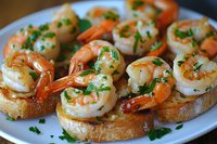 Grilled shrimp bruschetta appetizers garnished with fresh parsley and garlic butter sauce on toasted baguette slices served on white plate, close up view.