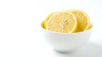 Fresh lemon halves in white ceramic bowl on clean background for healthy cooking and citrus fruit recipes in kitchen photography.