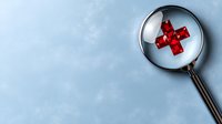 Magnifying glass focusing on red medical cross symbol against light blue background, emphasizing healthcare analysis and medical research concept.