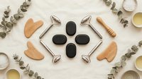 Spa wellness tools with gua sha stones, face rollers and massage accessories arranged on white wooden background for skincare routine and relaxation.