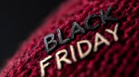 Black Friday text embroidered in black and gold thread on red textured fabric with dramatic lighting and shallow depth of field creating retail marketing atmosphere.