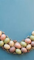 Pastel Easter eggs arranged in a curved wreath with dried flowers on a soft blue linen background, copy space for text.