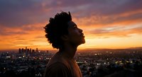 Young African American man in profile against vibrant sunset sky overlooking city skyline. Urban lifestyle portrait for wellness and inspiration content.