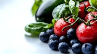 Fresh organic produce with water drops featuring ripe blueberries, vine tomatoes, and green vegetables against white background for healthy eating concept.