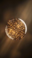 Transparent glass sphere filled with glowing golden light particles floating inside, isolated on warm brown blurred background for design and creative projects.