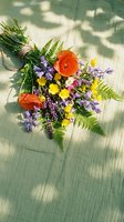 Wild flower bouquet with orange poppies, purple lupines, yellow buttercups and green ferns on wooden deck with natural sunlight shadows.