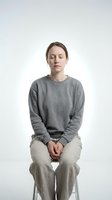 Young Caucasian woman sitting with eyes closed in meditation pose wearing gray sweatshirt on white background for mindfulness and wellness concepts.