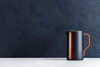 Modern black and orange metal pitcher on white surface against dark background, minimalist kitchen design composition for contemporary home decor and styling.