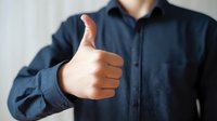 Businessman in navy blue shirt showing thumbs up gesture, conveying approval and positive feedback in professional setting.
