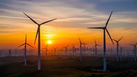 Wind turbines generating renewable energy at sunset with dramatic orange sky and rolling landscape creating sustainable power solution.