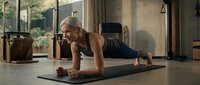 Young athletic blonde woman doing plank exercise on yoga mat in modern home gym with large windows and natural lighting for fitness training.