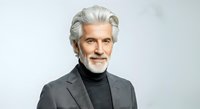 Senior man with white hair and beard, wearing gray blazer and black turtleneck, isolated on white background. Suitable for corporate, business, and professional design projects.