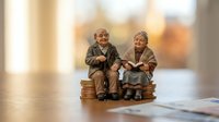 Elderly couple figurines sitting on stack of coins representing retirement savings, pension planning and financial security for senior citizens.