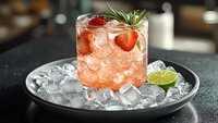 Fresh strawberry cocktail with lime, rosemary garnish and ice cubes served on black plate. Pink summer drink with fresh berries for bar menu.