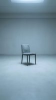 Single gray upholstered chair positioned in minimalist empty room with concrete floor and overhead skylight, conveying solitude and modern interior design concepts.