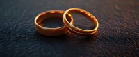 Two golden wedding bands interlocked on dark textured surface, symbolizing marriage commitment and eternal love for wedding and engagement designs.