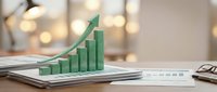 Green arrow and bar chart showing upward growth trend on financial documents with warm bokeh lights in modern office setting for business success presentations.