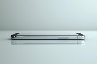 Modern smartphone shown in side view on reflective glass surface, highlighting sleek metallic frame and minimalist design profile against light background.