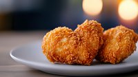 Crispy heart-shaped fried chicken pieces on white plate with soft bokeh background, golden brown breading texture creates romantic fast food presentation.