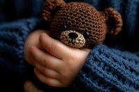 Cozy knitted brown teddy bear head held by small hands in warm blue sweater sleeve, creating intimate and tender childhood moment against dark background.