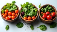Fresh organic cherry tomatoes and green salad leaves in wooden bowls on light background, healthy Mediterranean ingredients for cooking vegetarian meals.