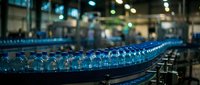 Conveyor line with filled water bottles moving through industrial beverage production facility with blurred factory background and equipment.