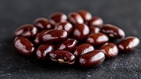 Dark chocolate covered almonds scattered on black stone surface with rich glossy coating and natural lighting, perfect for food photography and packaging.