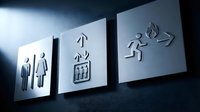 Modern metallic wayfinding signage system with restroom, elevator and emergency exit symbols mounted on dark wall with dramatic lighting for commercial spaces.
