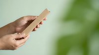 Close-up of hands holding wooden stick against blurred green background. Suitable for eco-friendly, natural product, sustainability, and educational content.