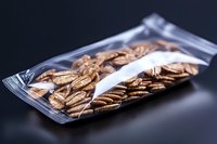 Fresh roasted coffee beans in transparent vacuum sealed packaging on dark background, selective focus highlighting aromatic whole beans for commercial use.