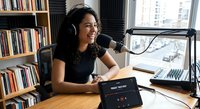 Young Asian woman podcaster smiling while recording in home studio with microphone, headphones and laptop. Professional broadcasting setup for content creation.