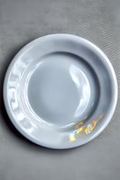 Clean white ceramic plate with subtle gold accent detail on gray textured background, photographed from above. Minimalist tableware for food presentation.