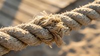 Frayed natural rope with worn fibers breaking apart, showing texture and deterioration. Concept of weakness, breaking point, stress and fragility.