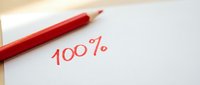 Red pencil writing 100 percent on white paper showing perfect score achievement for academic success and educational excellence concepts.