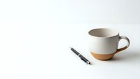 Minimalist workspace with ceramic coffee mug and black pen on clean white surface for business branding and office design concepts.