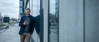 Confident mature businessman with smartphone standing outside modern office building in urban business district.