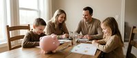 Caucasian family with two children planning household budget at dining table with piggy bank, calculator and financial documents in bright home interior.