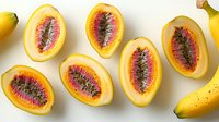 Fresh yellow banana passionfruit halves with vibrant pink flesh and black seeds arranged on white background, showcasing tropical fruit cross sections for food design.