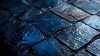 Dark cobblestone pavement with wet glossy surface reflecting blue night light, creating dramatic urban texture with geometric pattern and moody atmosphere.