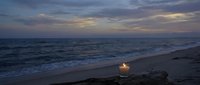 Peaceful ocean beach at twilight with glowing candle on driftwood creating romantic atmosphere for meditation and relaxation moments.