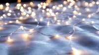 Glowing fairy lights creating magical bokeh effect on soft blue fabric surface, warm white LED string lights illuminate cozy winter atmosphere.